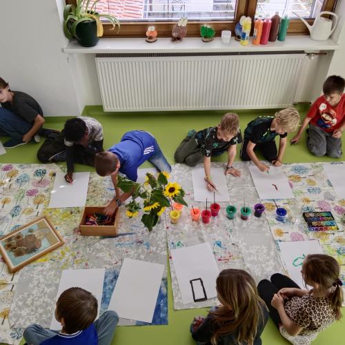 Kinder am Boden sitzend und beim Malen von Sonnenblumen